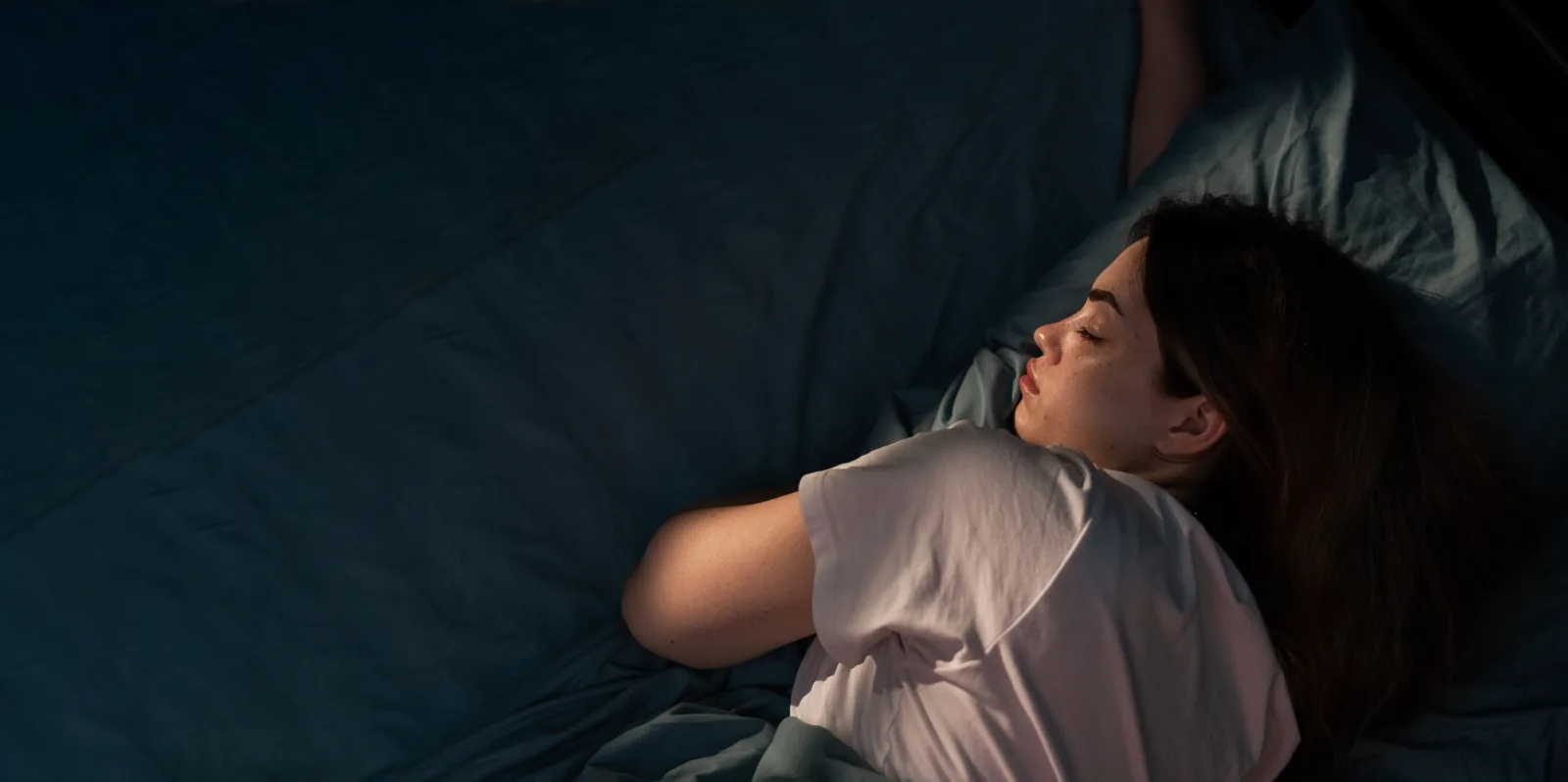 Persona dormida con un reloj inteligente en la muñeca, en una habitación en penumbra